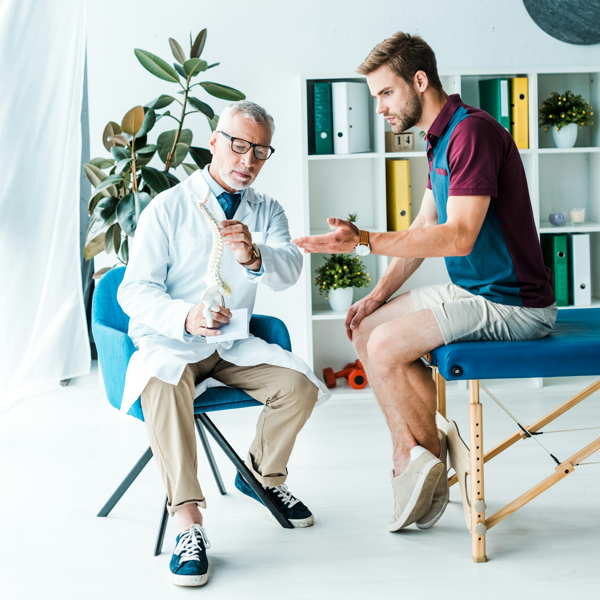 handsome bearded man gesturing while looking at spine model near doctor in glasses