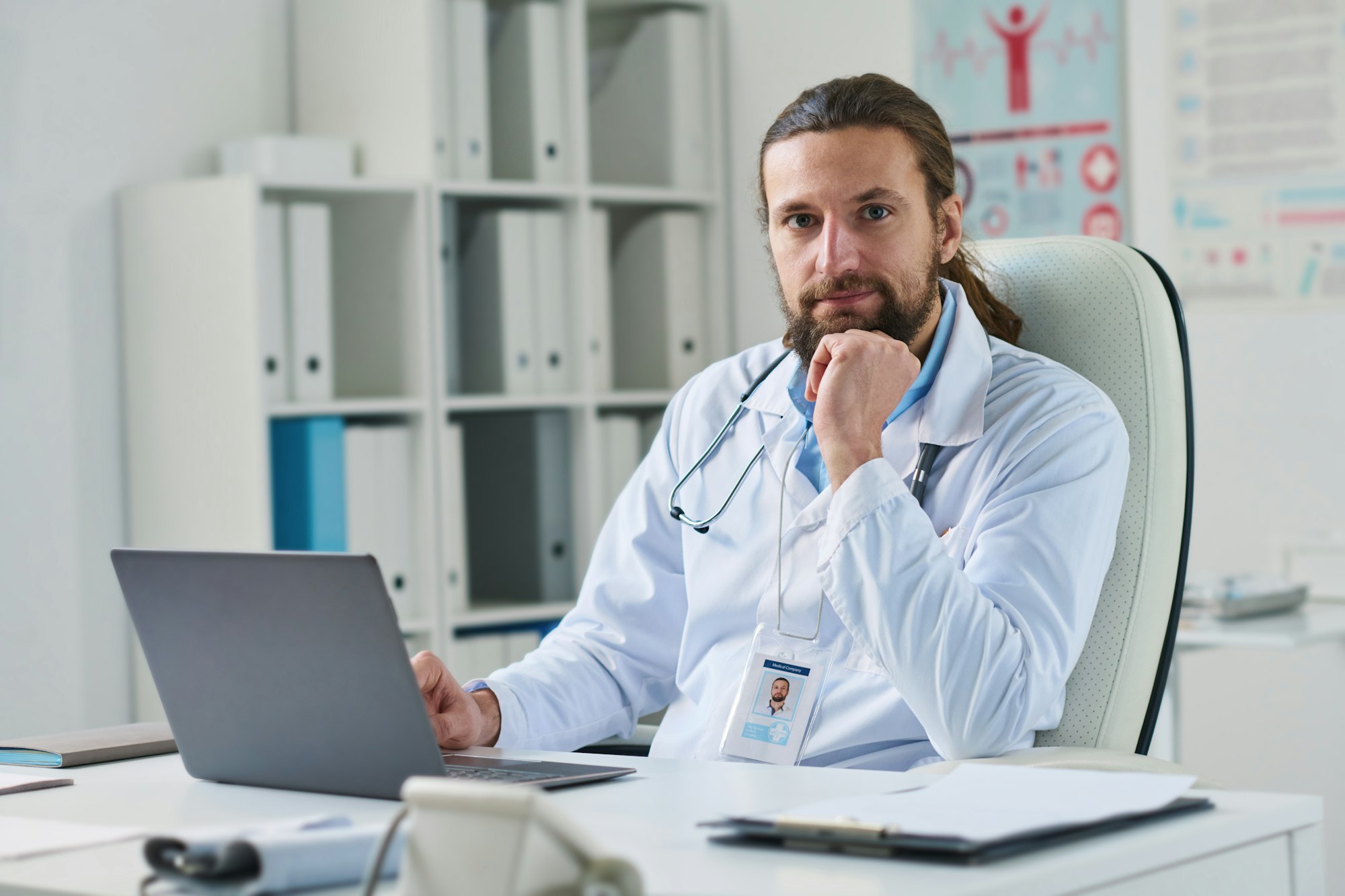 Young successful male clinician sitting by workplace in front of laptop