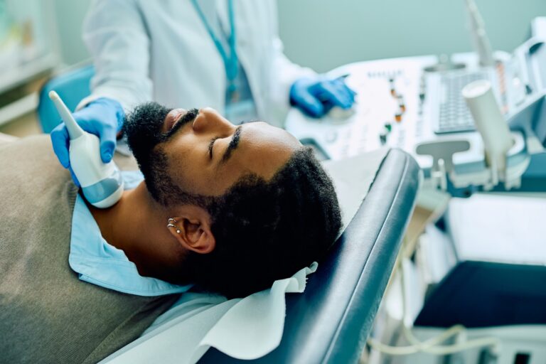 African American man having thyroid exam with ultrasound at doctor's office.