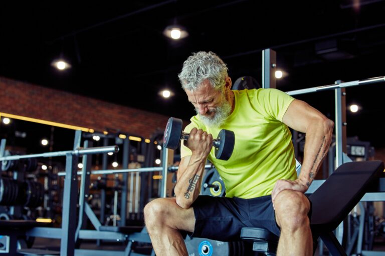 Getting strong arms. Focused mature man in sportswear lifting heavy dumbbells and pumping his